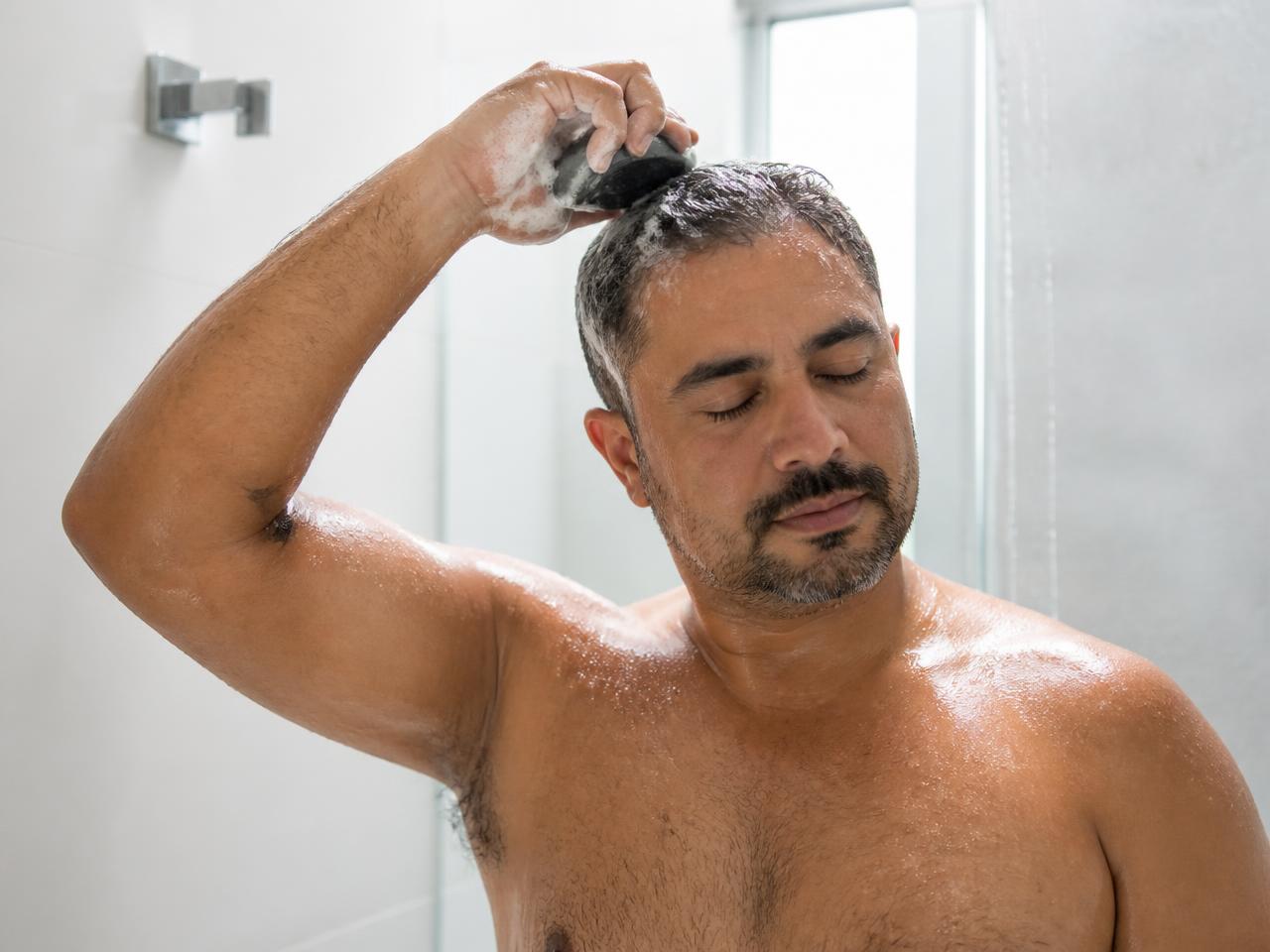 Homem aplicando o shampoo em barra no cabelo molhado